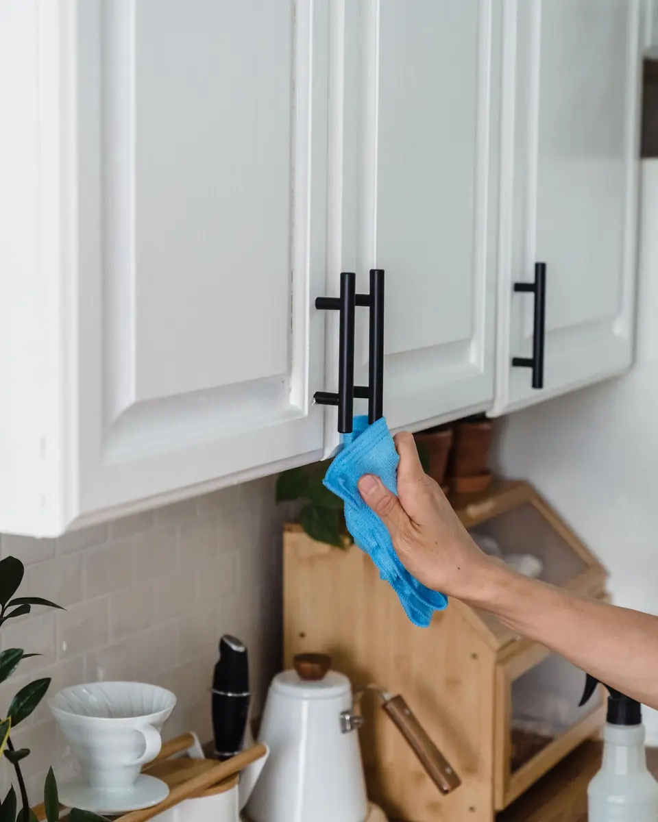 Hand wiping a kitchen cupboard handle with a blue cloth