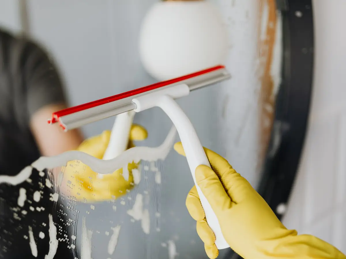Gloved hand pulling a squeegee across wet shower glass